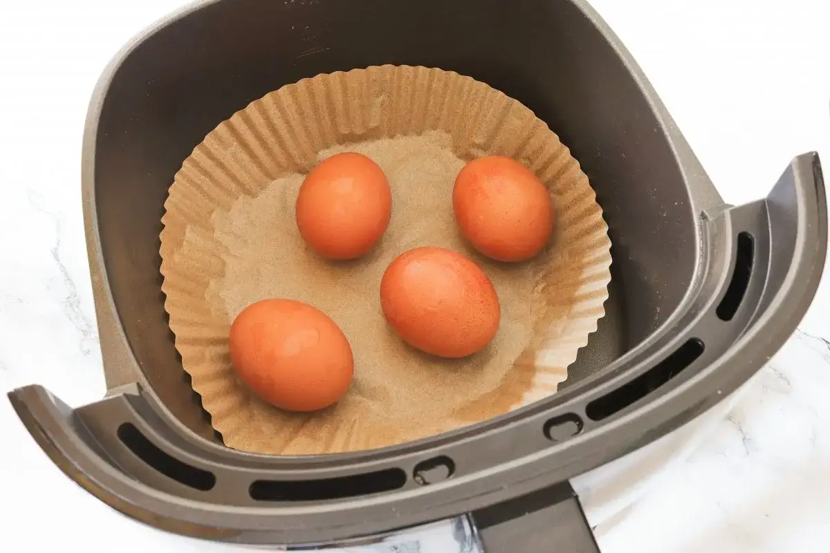 Cuatro huevos listos para convertirse en un delicioso huevo duro airfryer, colocados sobre papel de hornear en la cesta de la freidora de aire.