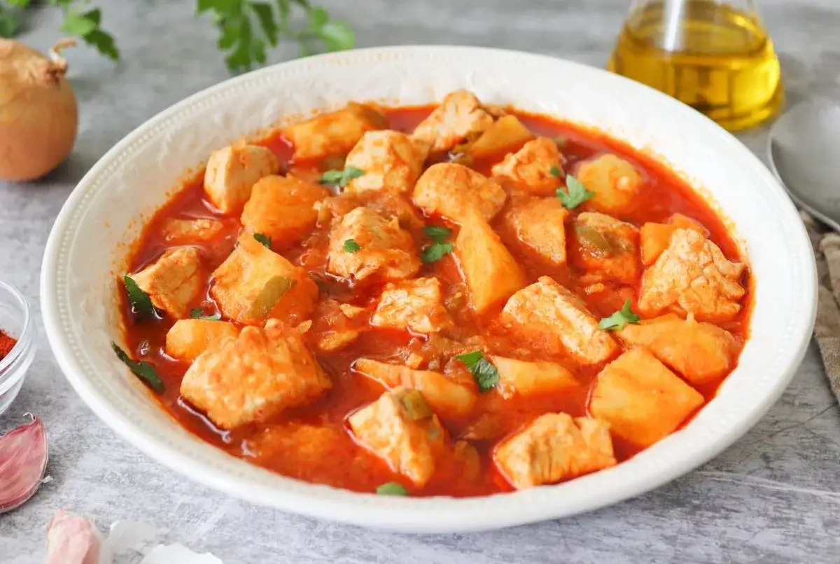 Un sabroso marmitako de bonito con patatas y pimientos en una cazuela blanca, listo para disfrutar.