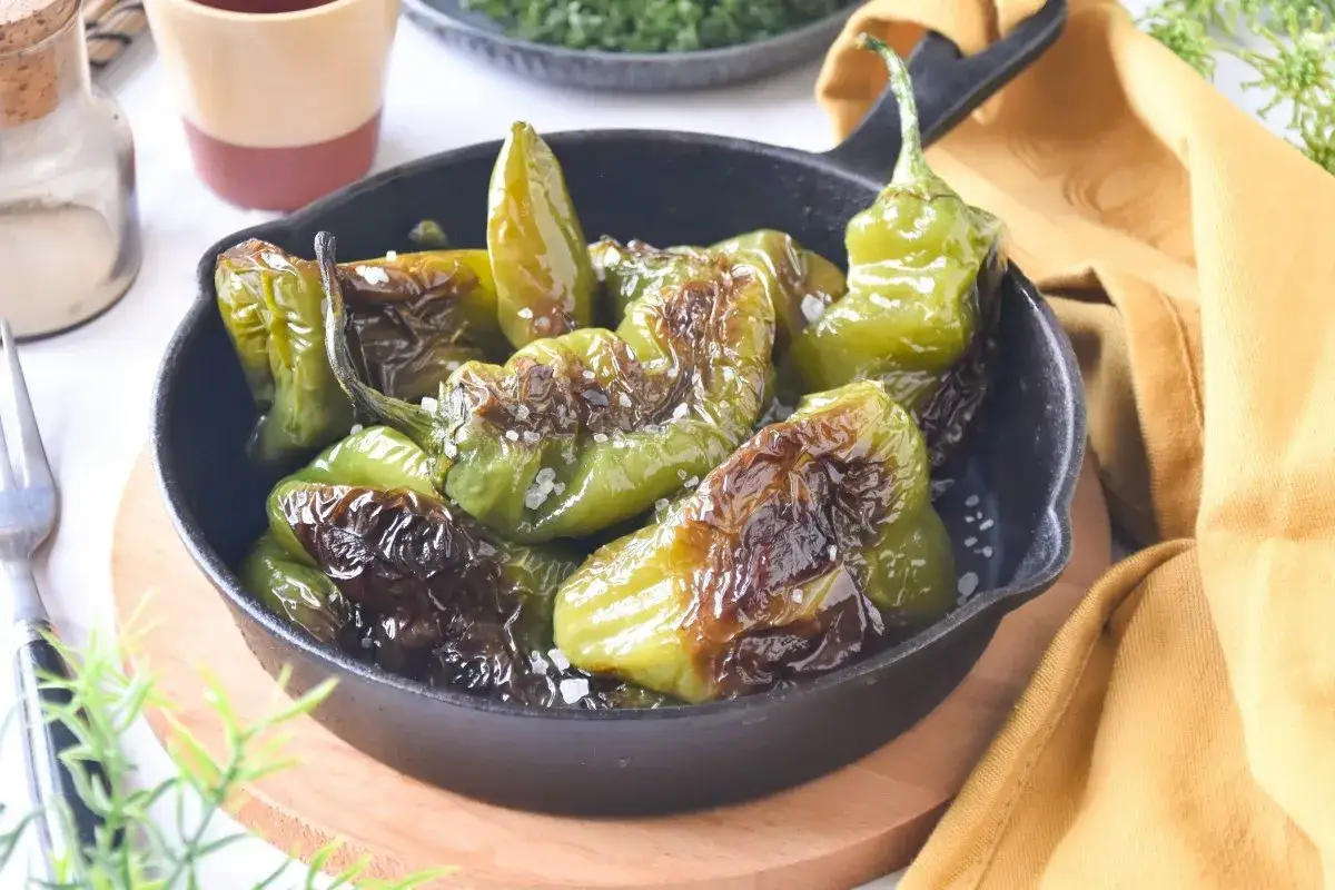 Pimientos fritos reci&eacute;n hechos, dorados y salpicados de sal marina, servidos en una sart&eacute;n de hierro fundido.