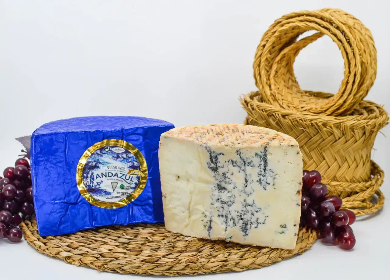 Queso azul Andazul, con sus distintivas vetas, envuelto en azul brillante y acompañado de uvas. Descubre sus propiedades.