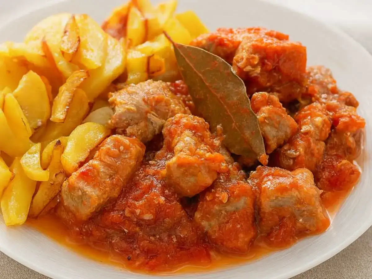 Sabroso magro con tomate, trozos de carne tierna en salsa roja, acompañados de patatas fritas doradas.