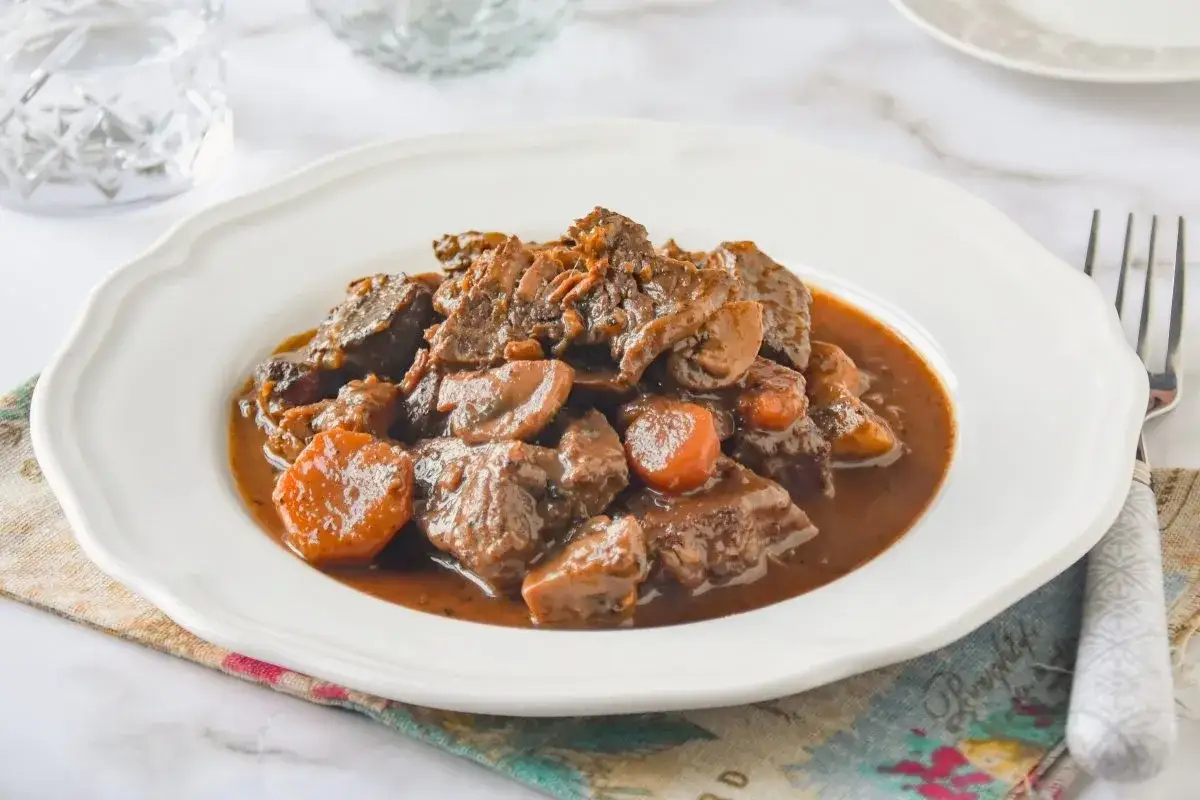Un plato de ragout de ternera con zanahorias y champiñones en una salsa oscura y rica.