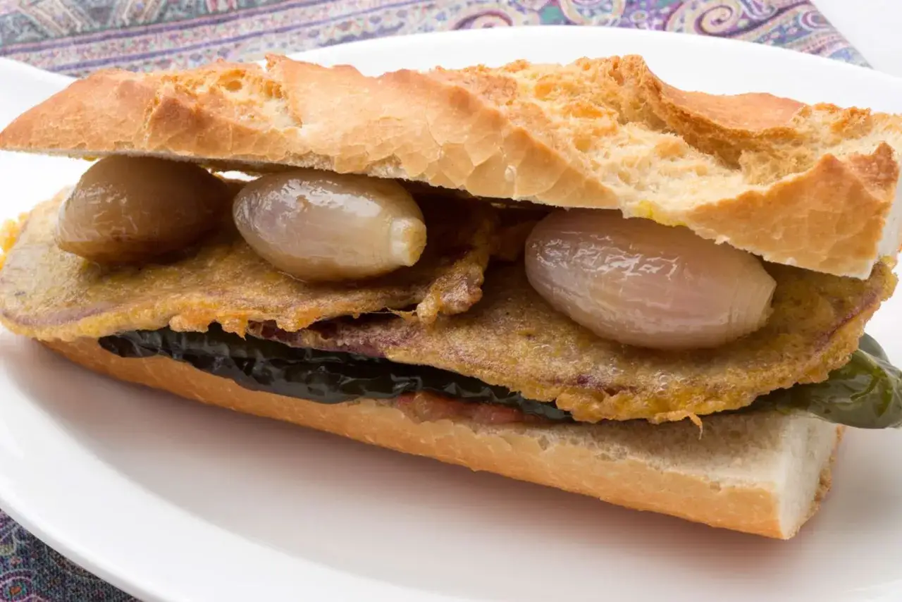 Un bocadillo de pepito de ternera con cebolla caramelizada y pimientos verdes.