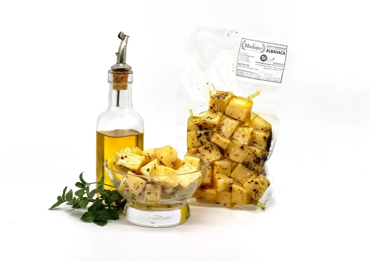 Queso curado de oveja en aceite de oliva con albahaca, servido en un cuenco y envasado al vacío, junto a una botella de aceite.
