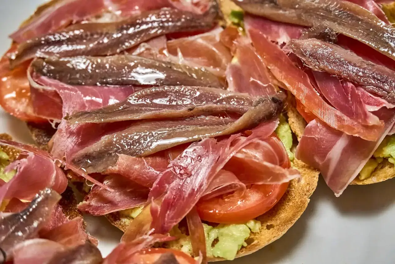 Tostadas con aguacate, tomate, jam&oacute;n y anchoas. Un aperitivo perfecto para tus recetas con anchoas.