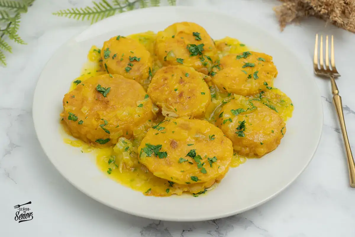 Patatas a la importancia, doradas y jugosas, servidas en una salsa amarilla con perejil picado. Un plato que demuestra la importancia de las patatas en la cocina.