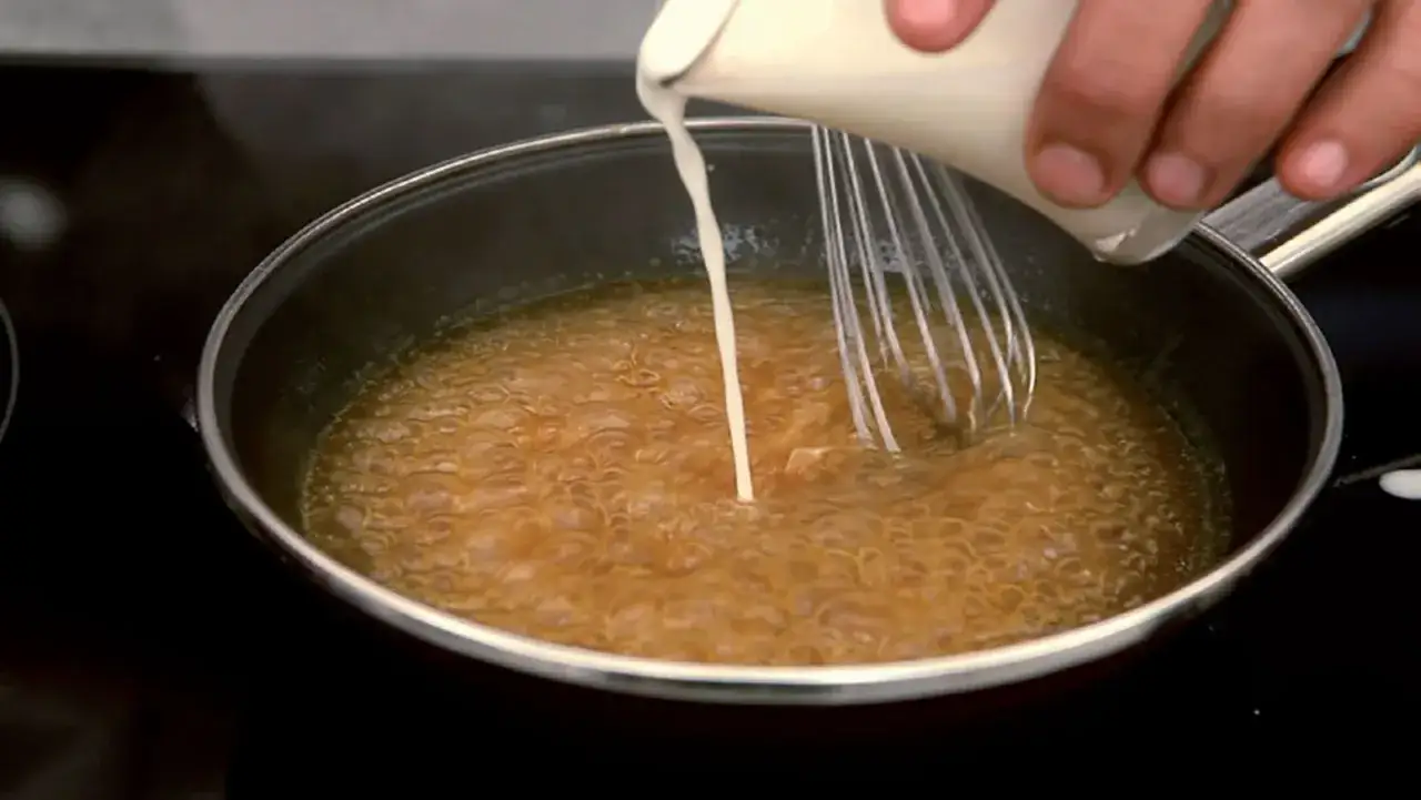 Se vierte crema en una sartén con líquido burbujeante, como si se preparara una salsa con fécula de maíz.