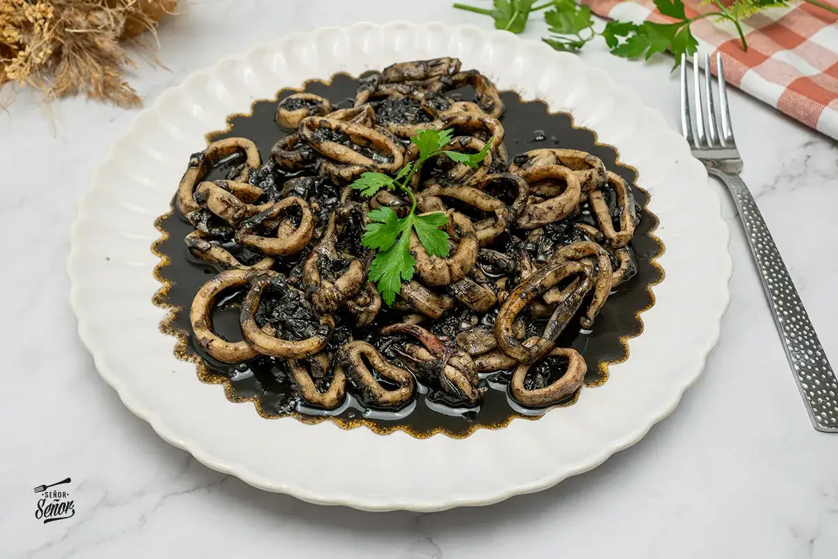 Calamares en su tinta, un plato tradicional espa&ntilde;ol, servido en un plato blanco con un tenedor y perejil fresco.