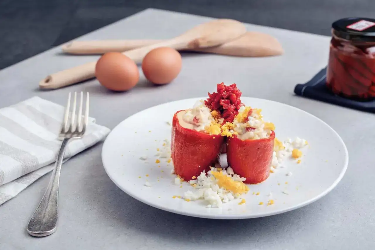 Dos pimientos del piquillo rellenos de ensaladilla, decorados con huevo duro picado y trocitos de pimiento rojo.