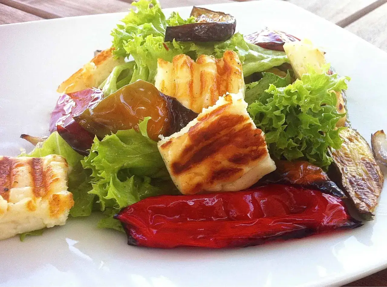 Ensalada fresca con trozos de ser halloumi a la parrilla, pimientos rojos asados y berenjena sobre lechuga crujiente.