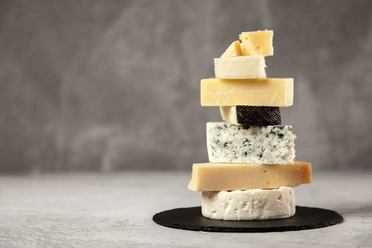 Torre de quesos variados, incluyendo un queso azul que puede ser beneficioso para la flora intestinal.