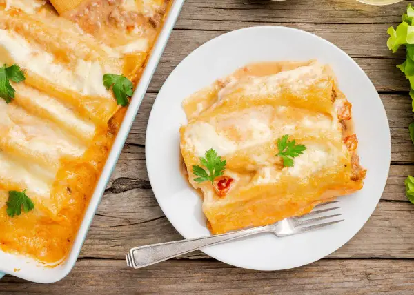 Canelones de atún gratinados, cubiertos de salsa y queso, servidos en un plato blanco con un tenedor.